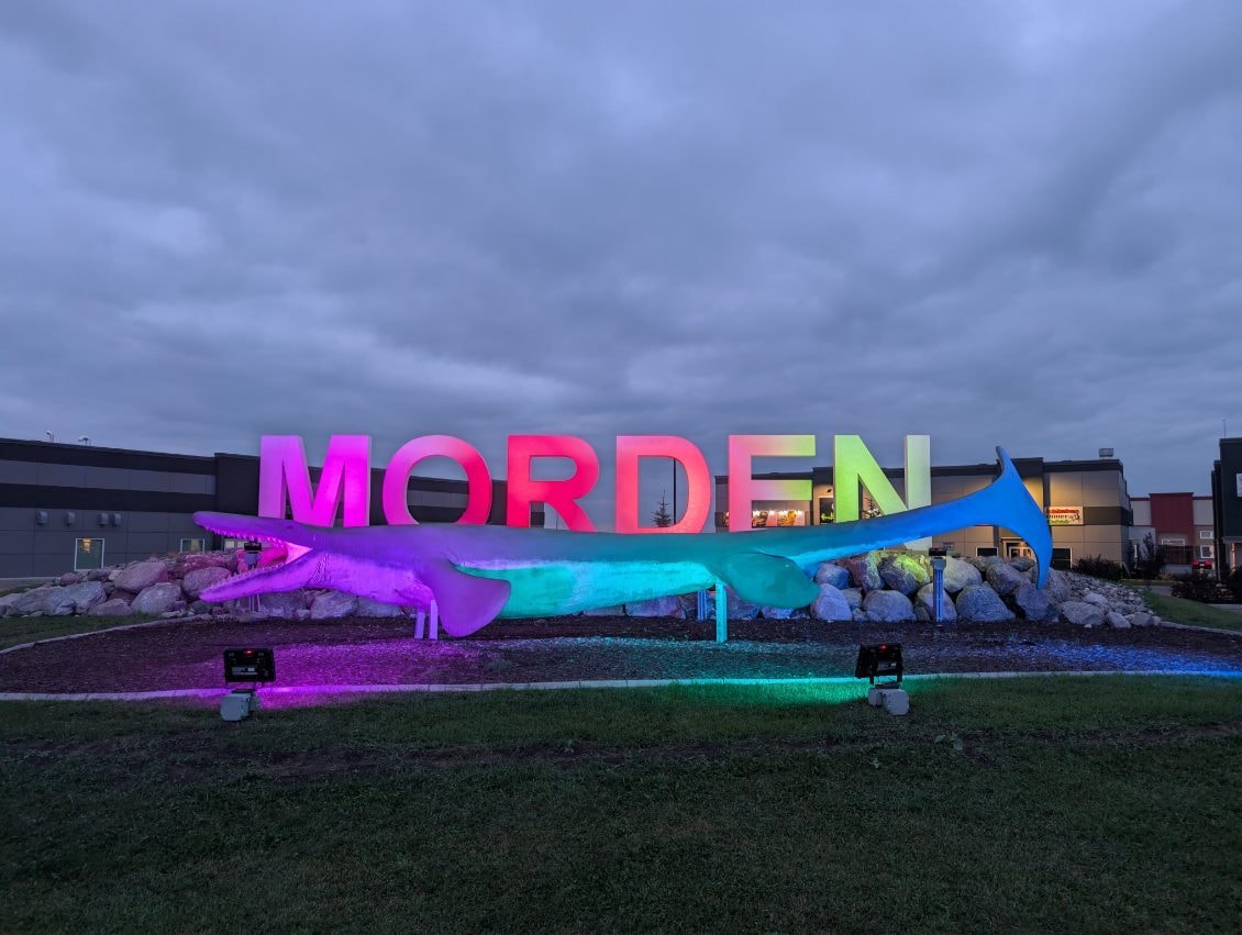 Morden city sign and mosasaur sculpture illuminated with colourful lighting at night